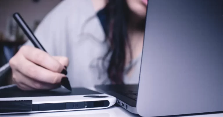 A digital designer holding her graphics tablet beside the laptop